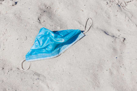 Used discarded medical protective mask on the beach sand. Sea beach garbage and pollution.の写真素材