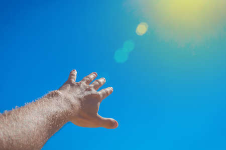 The guy stretched his hand forward towards the blue sky and the sun. The concept of freedom.の写真素材