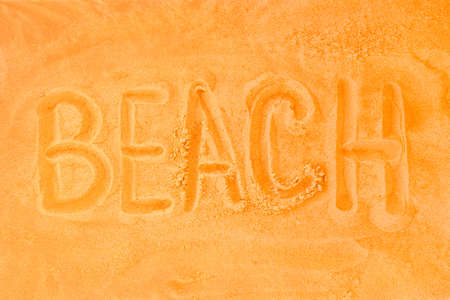 The word beach is written on a sand orange background. Sign or symbol of the beach concept.の写真素材