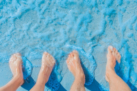 Women's and men's feet stand side by side on the sea beach in blue water, top view.の写真素材