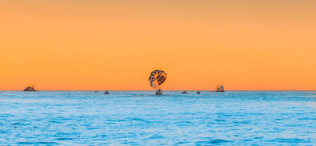 A boat with a parachute on the sky horizon with an orange sunset on the blue sea water background.の写真素材