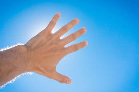 The guy stretched his hand forward towards the blue sky and the sun. The concept of freedom.の写真素材