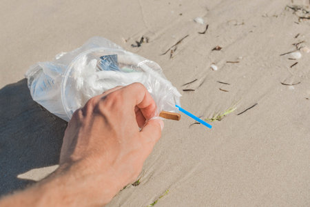Man's hand picks up or collects garbage on a seaside beach close-up.の写真素材