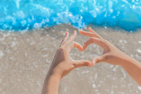The girl with both hands depicts a symbol and a sign of love and heart against the sea shore close-up.の写真素材
