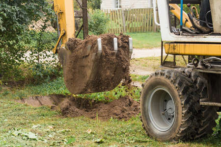 Excavation work on the construction site. A bucket of a bulldozer digs the ground with a grass close-up in an industrial area.の写真素材
