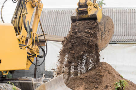 A bucket of excavator pours the ground into a heap against the background of a rural industrial zone. Bulldozer work on the construction site.の写真素材
