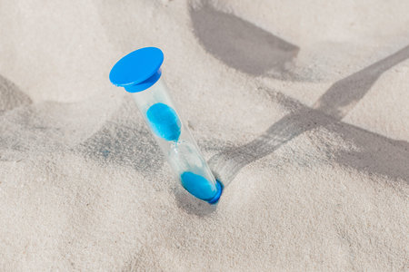 The hourglass is stuck in the beach sand close-up. The concept of the outgoing time.