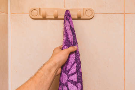 Man's hand takes an purple towel in the bathroom. Care and hygiene concept.の写真素材