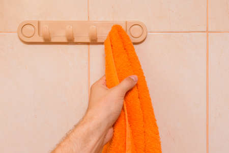 Man's hand takes an orange towel in the bathroom. Care and hygiene concept.の写真素材