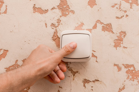 The man's hand turns off the light with an electric switch in a modern room interior background.の写真素材