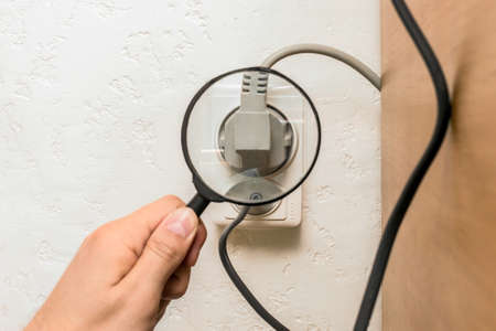 The hand of a male worker examines through a magnifying glass the connection of appliances in the house.の写真素材