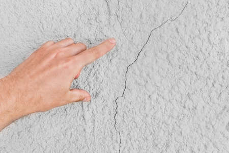 Male construction worker hand points cracks on white wall background. Renovation concept.の写真素材