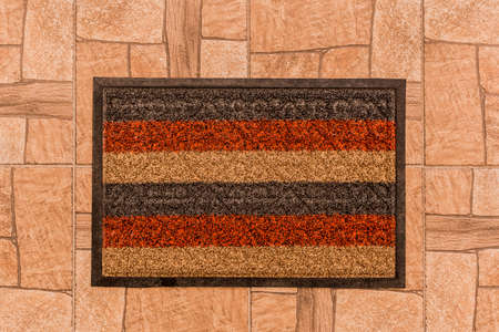 The rug for the feet of guests in the hallway on the background of a brown tiled floor texture background, top view.の写真素材