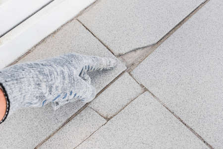 Hand of industrial worker in construction glove points on damaged gray tile background. Renovation concept.の写真素材