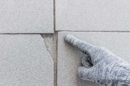 Hand of industrial worker in construction glove points on damaged gray tile background. Renovation concept.の写真素材