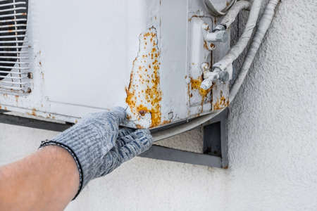 Hand of industrial worker in construction glove touching rust on old air conditioner against white wall background.の写真素材