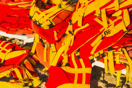 Red and yellow life jackets in a heap on the sea beach.の写真素材