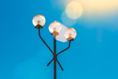 Street lighting element, lantern during the day in sunlight with glare against a blue sky.
