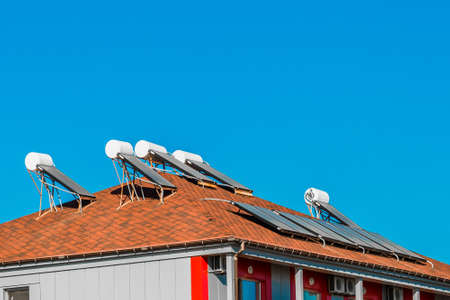 Solar water heater on the roof of a building against the background of the blue sky. Using solar energy to heat water.の写真素材
