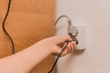 A female hand inserts or removes a plug from an outlet in a modern interior. Safe use of electrical...
