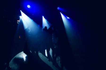 White spotlights in the dark with blue club lighting on the dance floor with people dancing near the bar. Nightlife concept, blurred background.の写真素材