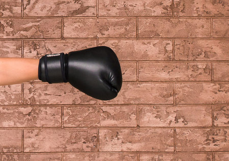 The hand of a guy in a black wrestling glove on a background of a brown brick wall. Boxing concept.の写真素材
