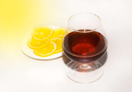 Cognac in a glass next to sliced lemon wedges on a plate. Alcohol and snacks concept.の写真素材