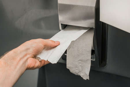 Man's hand takes or tears off toilet paper in a roll, close-up, soft focus.の写真素材