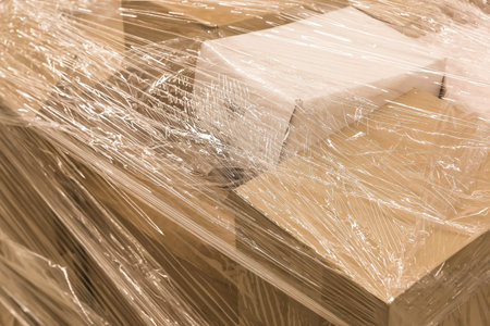 Cardboard boxes with goods or building materials and wrapped in packaging film, close-up.
