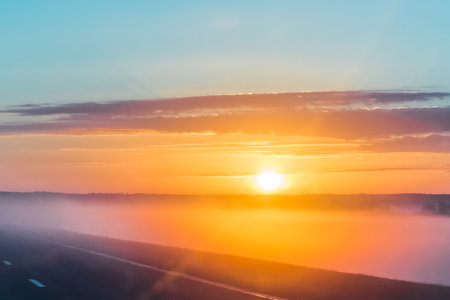Dawn with fog, foggy road. Beautiful landscape early in the morning with bright orange rising sun and clouds.の写真素材