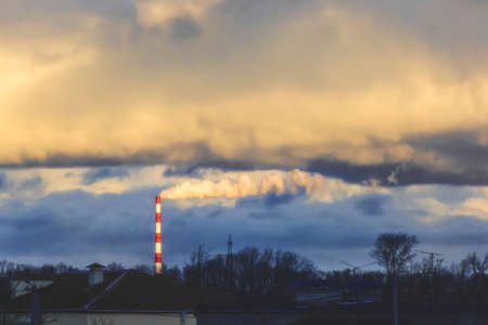 Environmental pollution problems and ecology concept. Yellow smoke at sunset comes from a chimney of an industrial enterprise or thermal power plant and carbon dioxide is released into the atmosphere.の写真素材