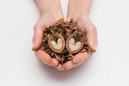 Woman holds out her hands with a bunch of peeled leftovers nuts and two halves of a walnut in the form of a heart on a white background, isolated. Nut concept.の写真素材