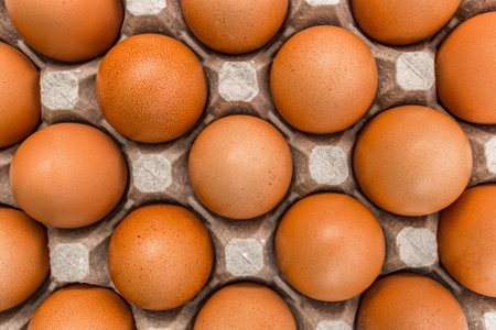 Raw chicken eggs in a cardboard tray with brown eggs background.
