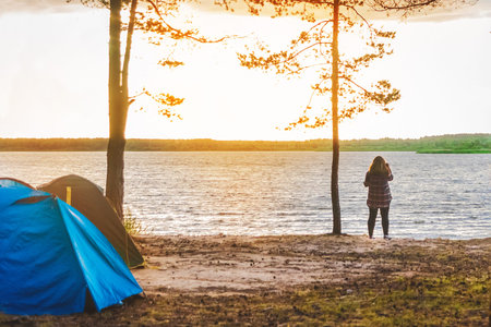 Silhouette of a girl on the background of the lake, a camp in the forest, travel and vacation in...