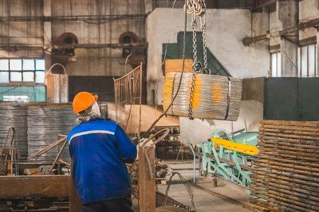 Worker in a reinforcement workshop in a helmet controls equipment for moving metal structures.