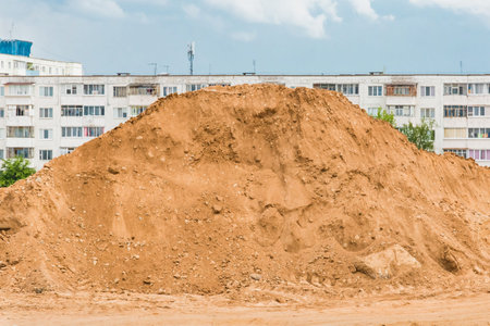 Large pile of sand nature material at a construction site against the background of old multi-storey...