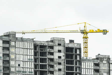 Tower yellow construction crane builds new concrete and cement city building on construction site.の写真素材