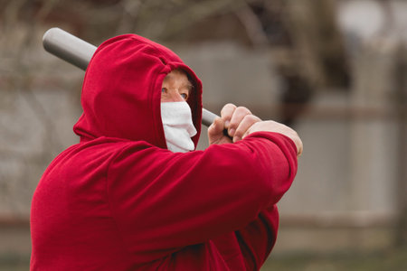Angry aggressive elderly man in protective safe medical mask swings baseball bat in the background...