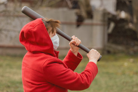 Angry aggressive elderly woman in protective safe medical mask swings baseball bat in the background...