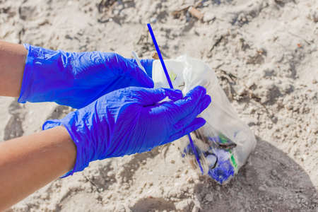 Hands of a girl in blue household gloves collect garbage in a bag on the beach close-up cleaning plan.の写真素材
