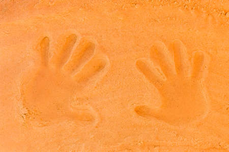Traces of male and female palm hands on orange beach sand close-up.の写真素材