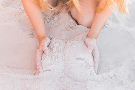 The hands of a young girl hold a pile of white sand close-up.の写真素材