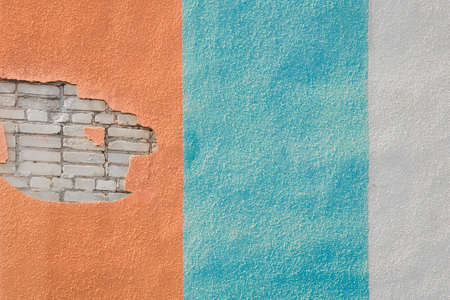 Peeling plaster on the colored facade of a modern building in the city. Repair or reconstruction of the wall of a city house.の写真素材