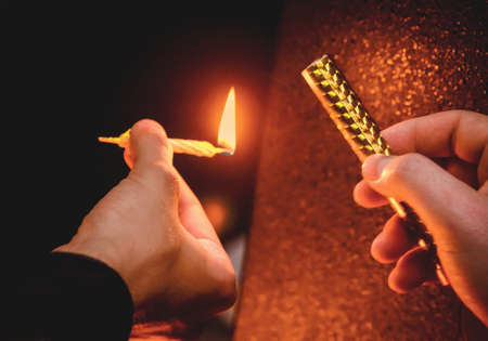 Man's hands are holding a small burning holiday candle and lighting a cold fountain candle, close-up.の写真素材