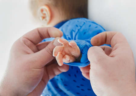 Dad's hands roll up sleeves on baby's hand, close-up. Newborn child in the hospital, love and care of the parent's dad.の写真素材