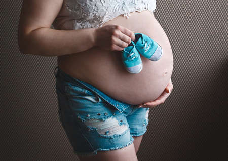 Hands of a pregnant girl hold belly and small baby booties, awaiting the birth of a baby.の写真素材