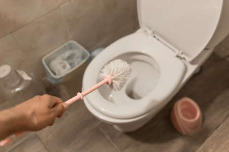 The guy's hand holds the toilet brush and cleans the toilet. The concept of home cleaning and hygiene in the bathroom.の写真素材