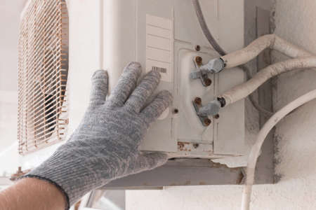 The hand of an air conditioner repair and maintenance specialist in a construction glove working with air-conditioned old equipment.の写真素材