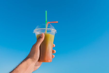 The guy's hand holds a colored chilled non-alcoholic cocktail against the background of the blue sky.の写真素材