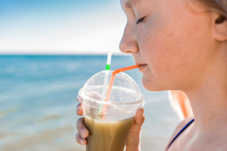 A young girl with blonde hair of European appearance, a teenager holds and drink a colored cold...